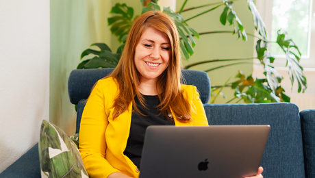 Kathrin Schönborn trägt einen gelben Blazer und arbeitet an ihrem Laptop auf dem Sofa
