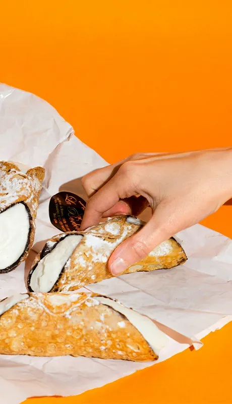 Eine Hand greift nach einem gefüllten Cannolo